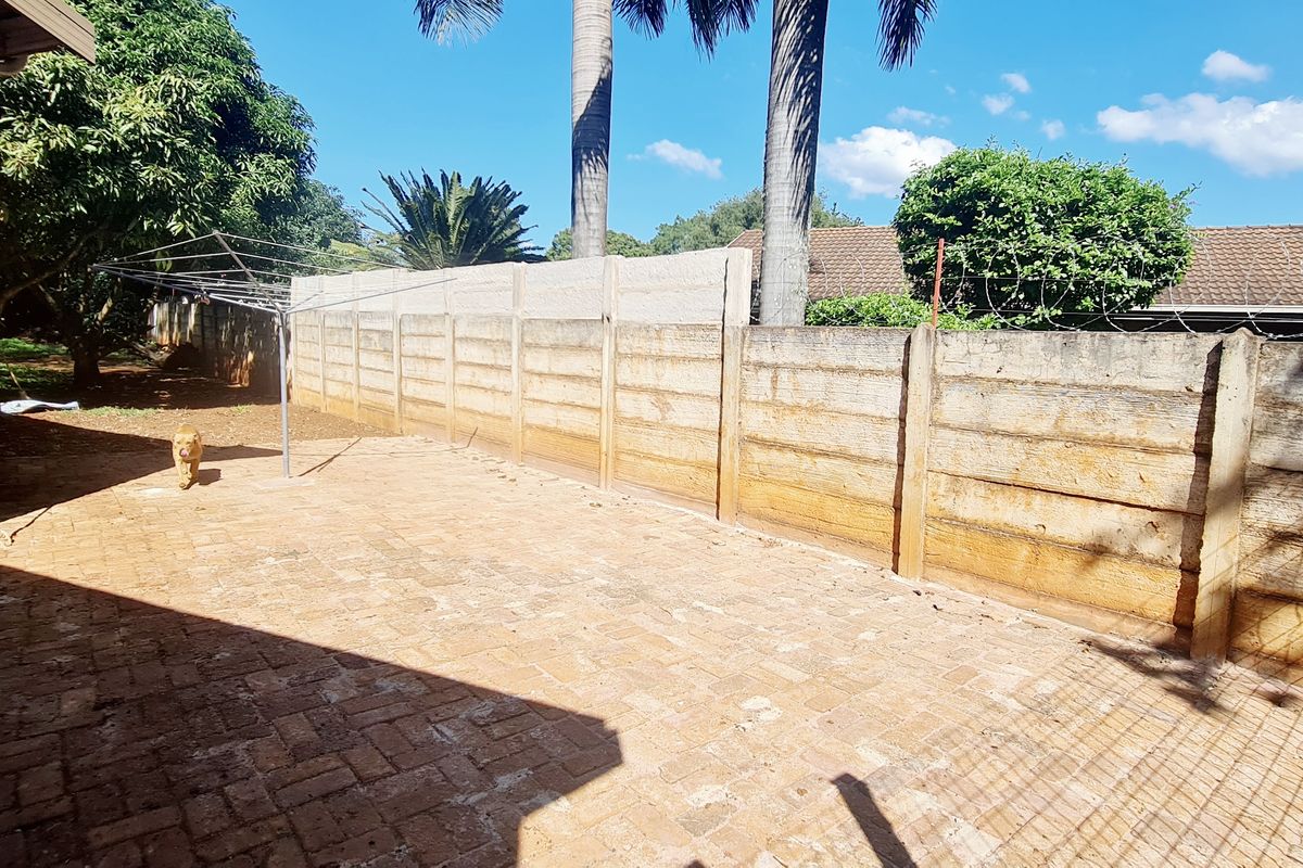 A rear exterior area featuring brick paving and a precast concrete boundary wall with security razor wire.