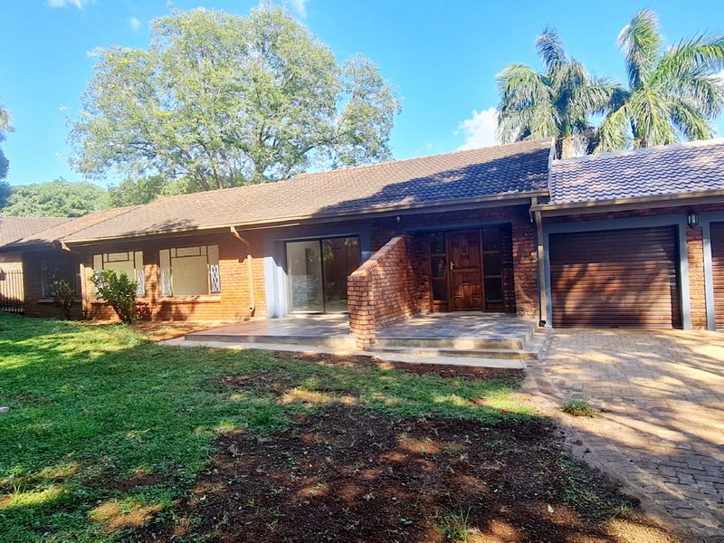 Front view of a single-story brick house featuring a double garage, paved driveway, and a covered entrance area set within a landscaped garden.