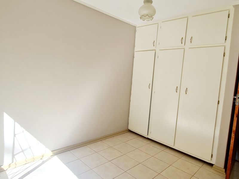 A bright, empty bedroom featuring tiled flooring and ample built-in cupboard storage space.