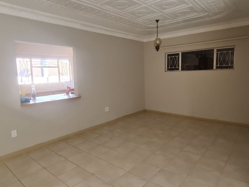 An empty living room featuring tiled flooring, decorative ceiling molding, and a convenient pass-through window connecting to the kitchen area.