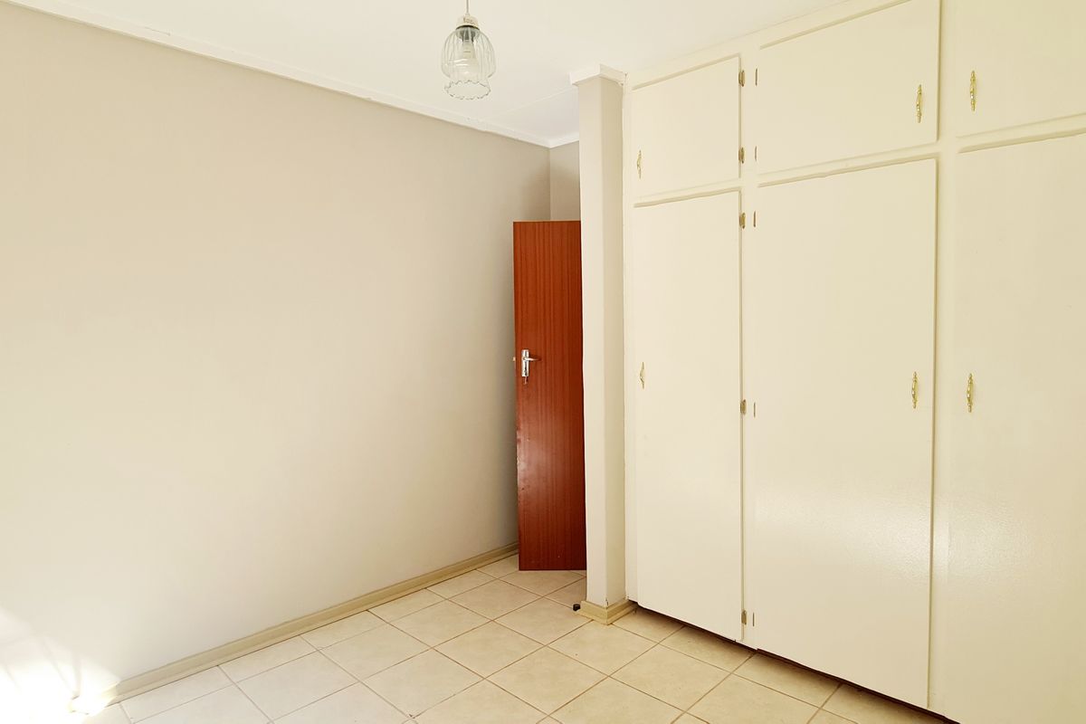 An empty bedroom featuring neutral walls, tiled flooring, and ample built-in cupboard storage space.