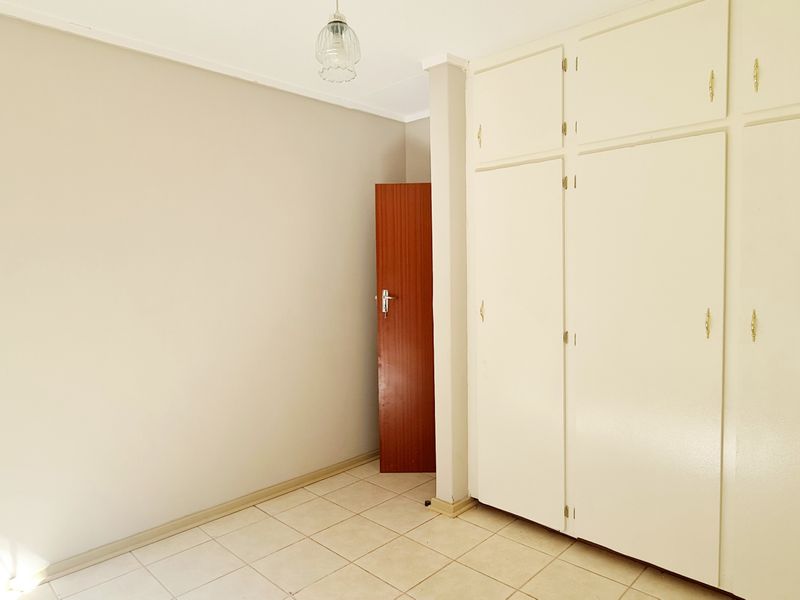 An empty bedroom featuring neutral walls, tiled flooring, and ample built-in cupboard storage space.