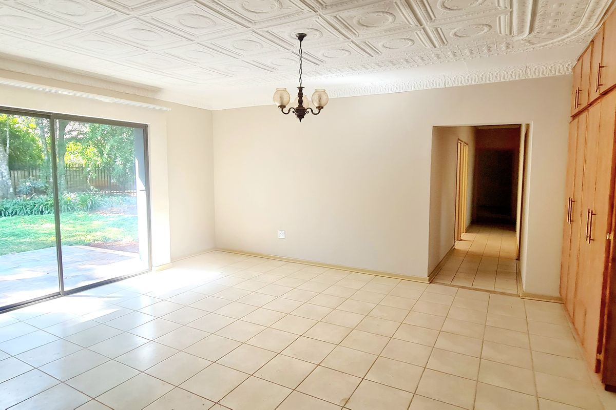 Spacious living area featuring tiled flooring, decorative ceiling tiles, built-in storage cupboards, and large sliding glass doors providing access to the garden.