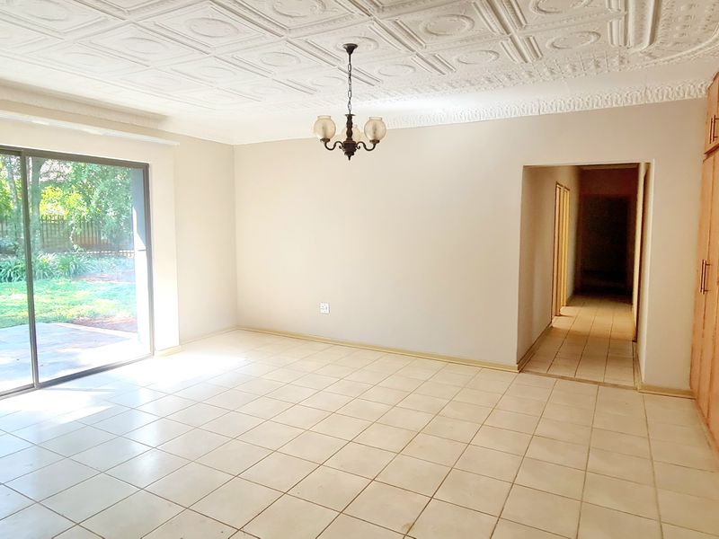 Spacious living area featuring tiled flooring, decorative ceiling tiles, built-in storage cupboards, and large sliding glass doors providing access to the garden.