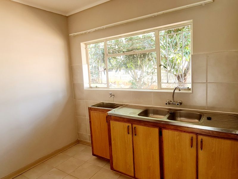 A functional scullery area featuring built-in wooden cabinetry, a stainless steel double sink, and tiled splashbacks, offering a practical space for utility and prep.