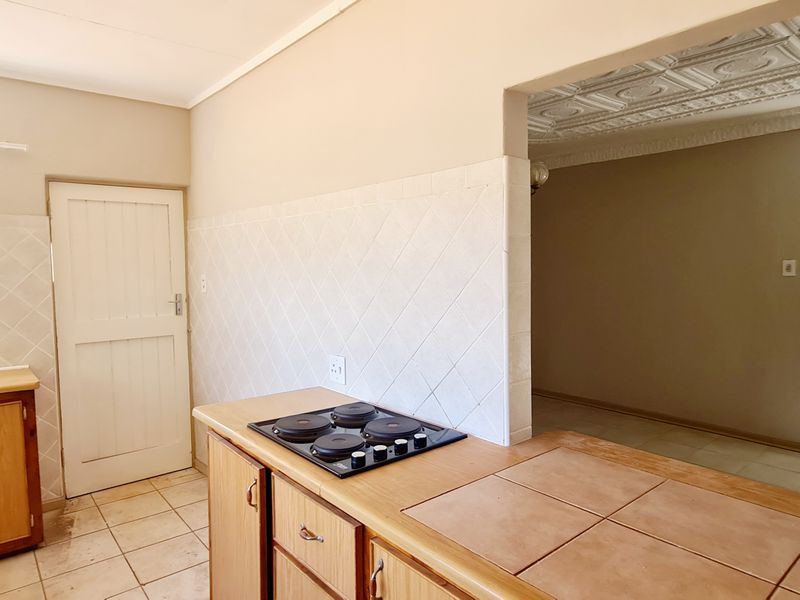 A functional kitchen featuring built-in wooden cabinetry, a tiled splashback, and an electric hob, with an open-plan layout connecting to the adjacent living area.