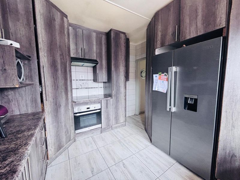A functional kitchen featuring wood-look cabinetry, tiled flooring, a built-in oven and hob, and a tiled backsplash.