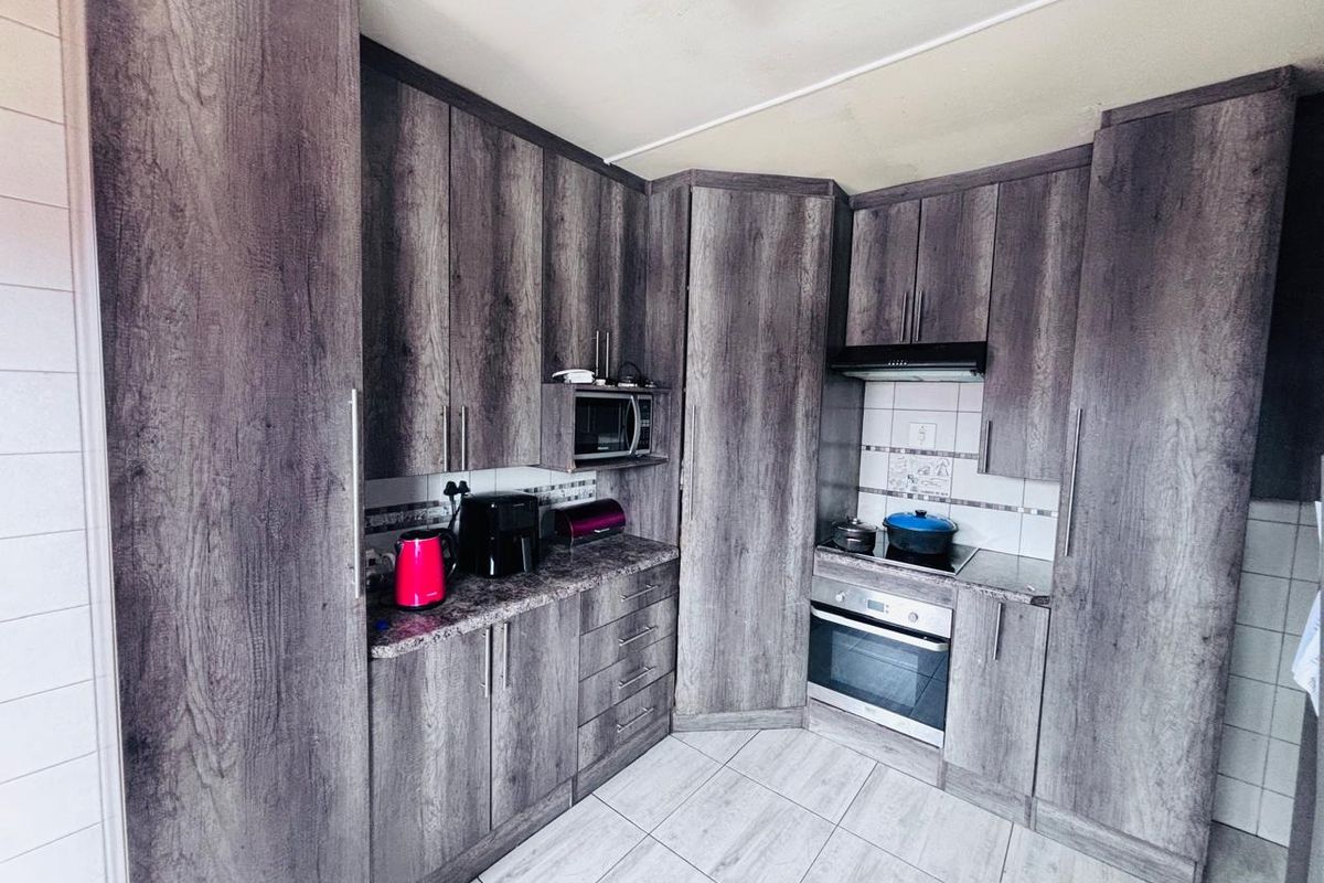 A functional kitchen featuring modern wood-look cabinetry, built-in oven and hob, extractor fan, and tiled flooring with a neutral backsplash.