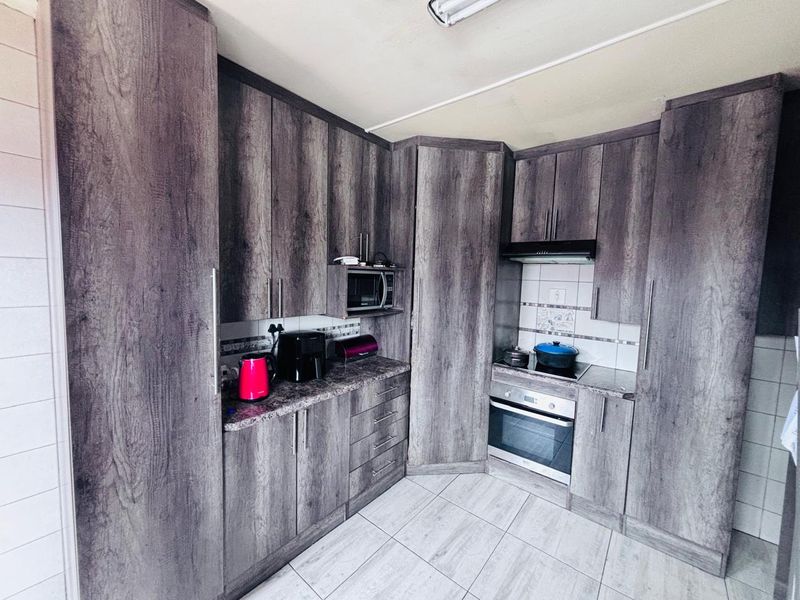 A functional kitchen featuring modern wood-look cabinetry, built-in oven and hob, extractor fan, and tiled flooring with a neutral backsplash.