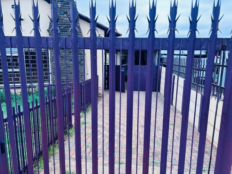 Front view of the property featuring a paved driveway and secure metal perimeter fencing with spikes.