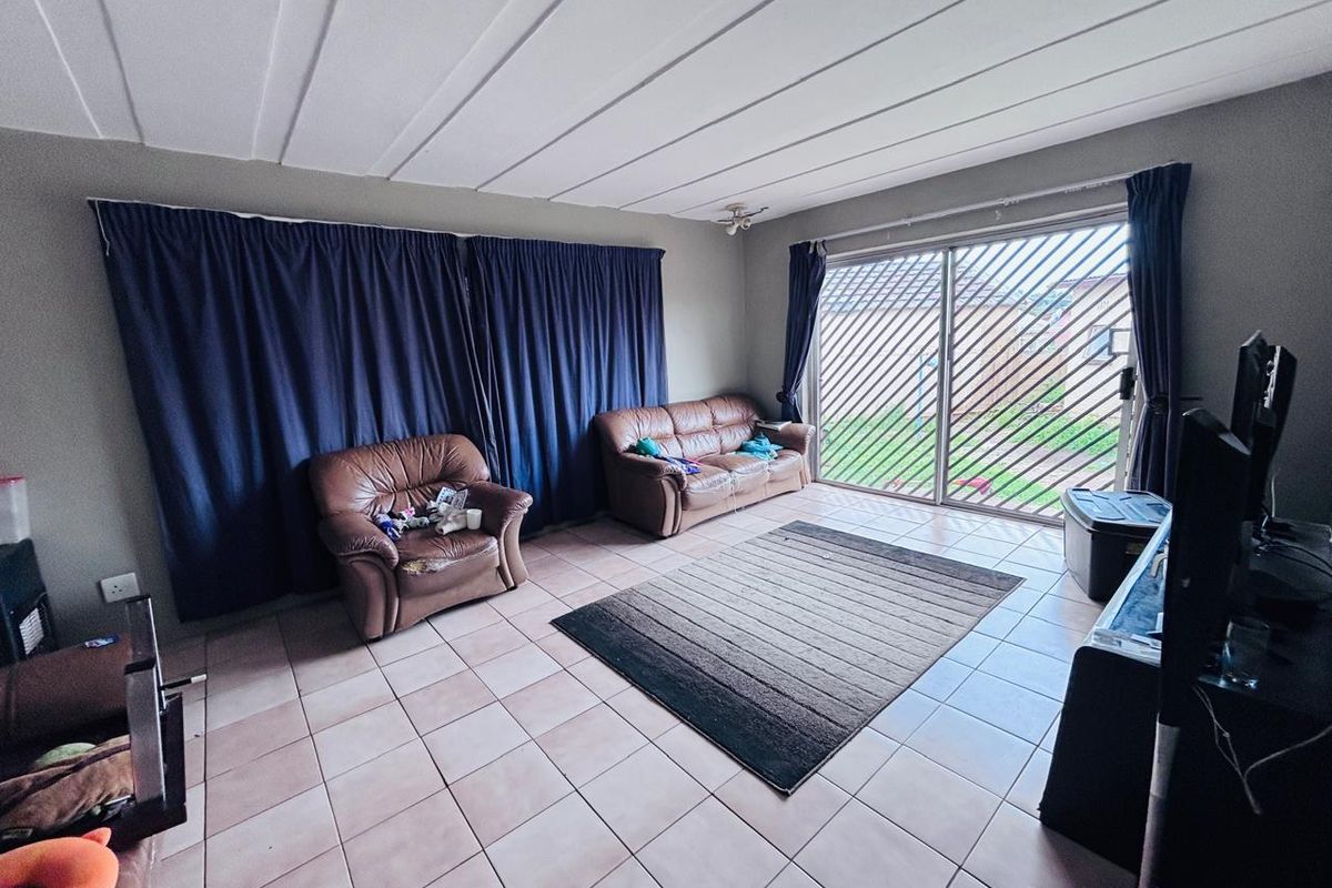 A living room featuring tiled flooring, a panelled ceiling, and a sliding glass door with a security gate leading to the garden.