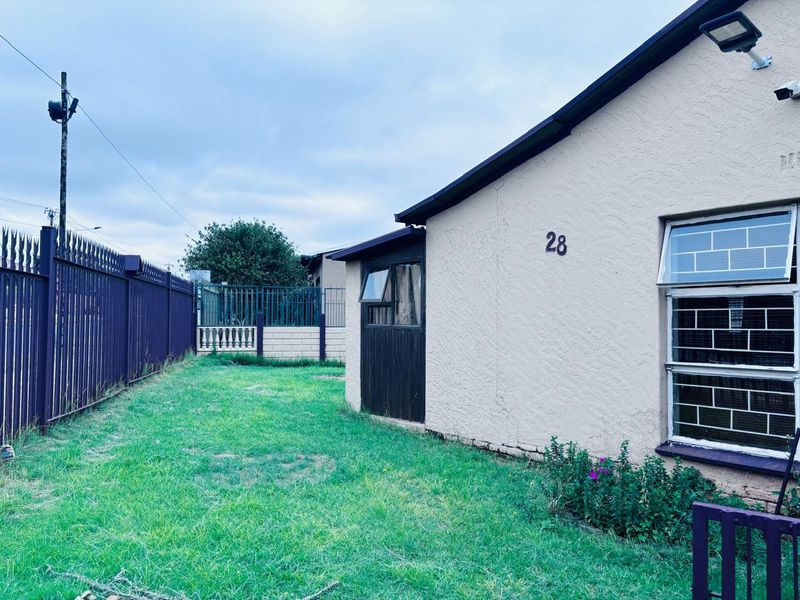 Rear exterior view of the property featuring a lawn, security fencing, and a side wall with security lighting and burglar-barred windows.