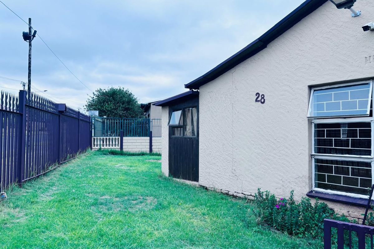 Rear exterior view of the property featuring a lawn, security fencing, and a side wall with security lighting and burglar-barred windows.