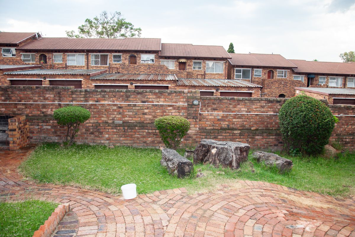 A rear view of the apartment complex featuring a private garden area with brick boundary walls, paved patio, and established shrubs.