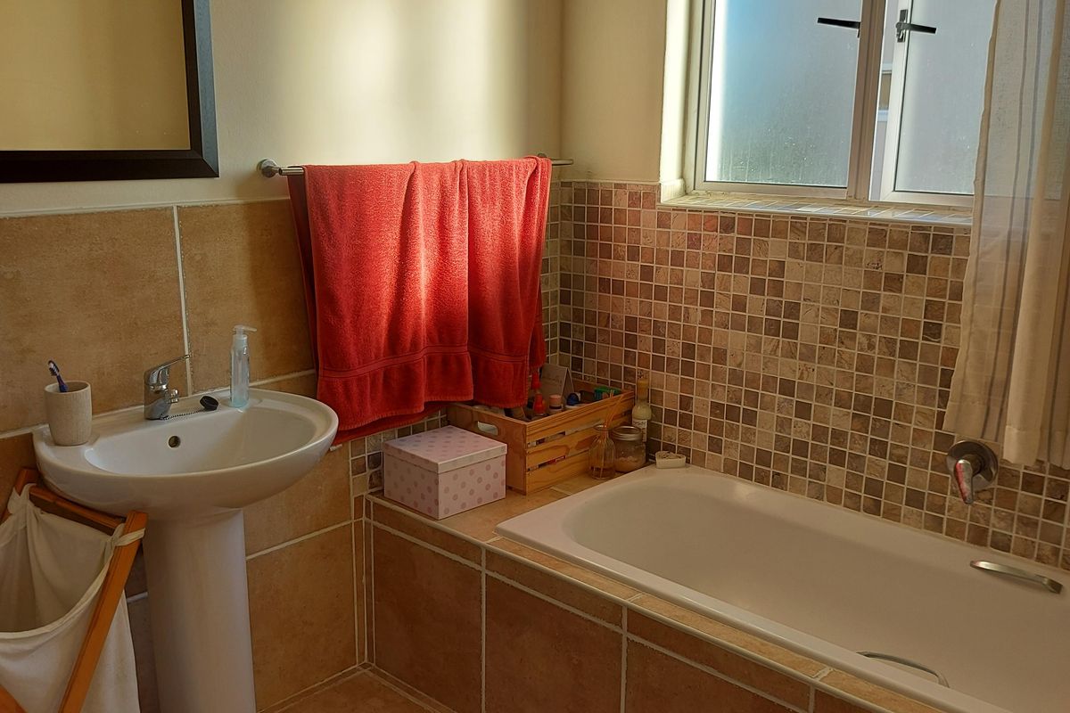 A functional bathroom featuring a pedestal basin, a built-in bathtub with tiled surround, and neutral floor tiling, illuminated by natural light from a frosted window.