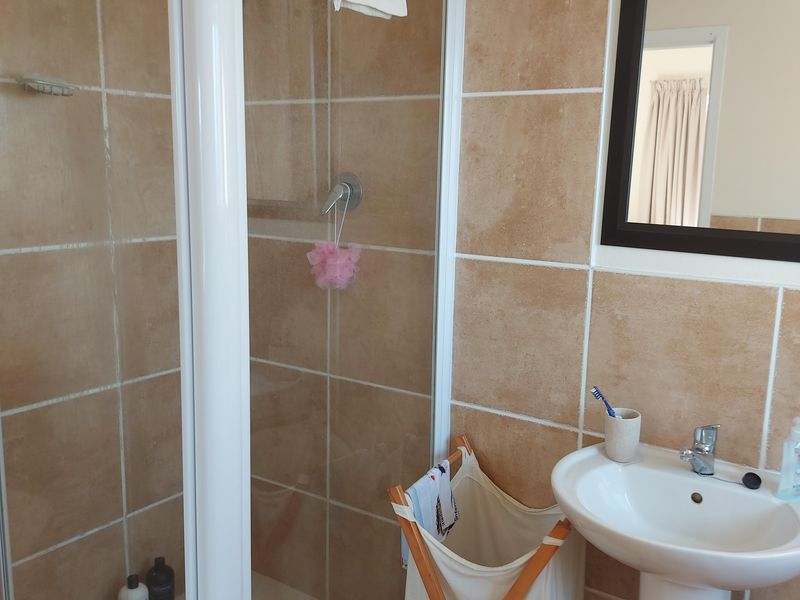 A functional bathroom featuring a glass shower enclosure, pedestal basin, and neutral wall tiling.