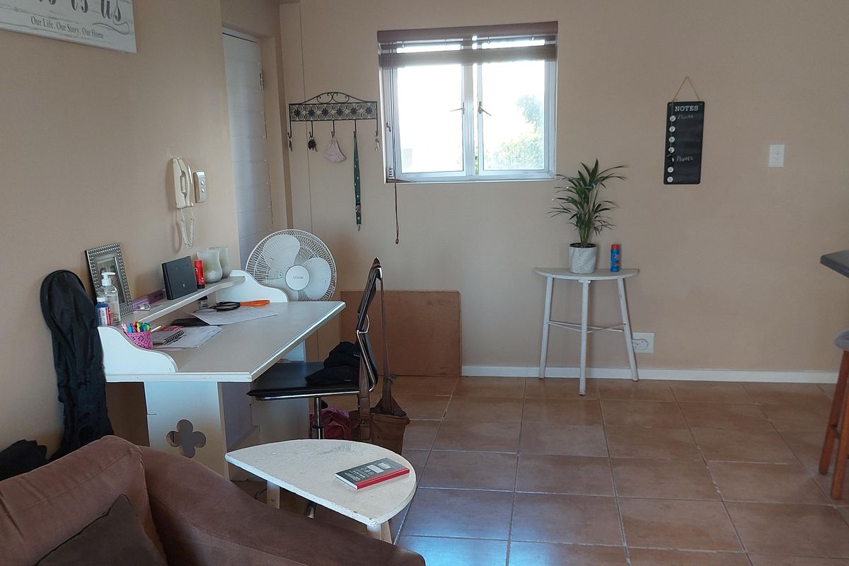 A living area featuring neutral wall tones, tiled flooring, and natural light from a window with fitted blinds.