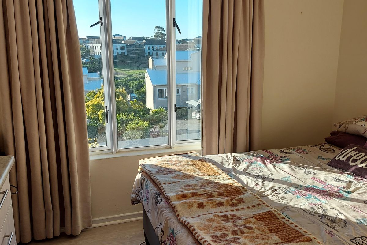 A bedroom featuring laminate flooring and a large window with natural light and neighborhood views.