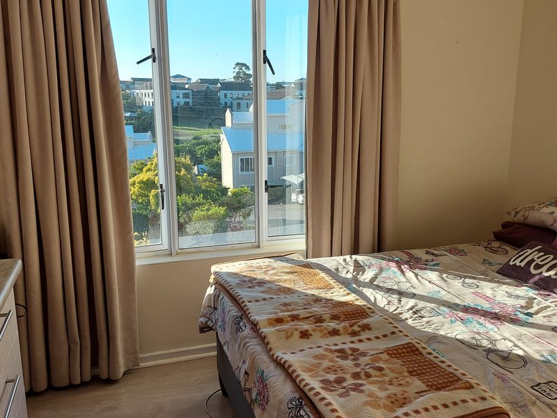 A bedroom featuring laminate flooring and a large window with natural light and neighborhood views.