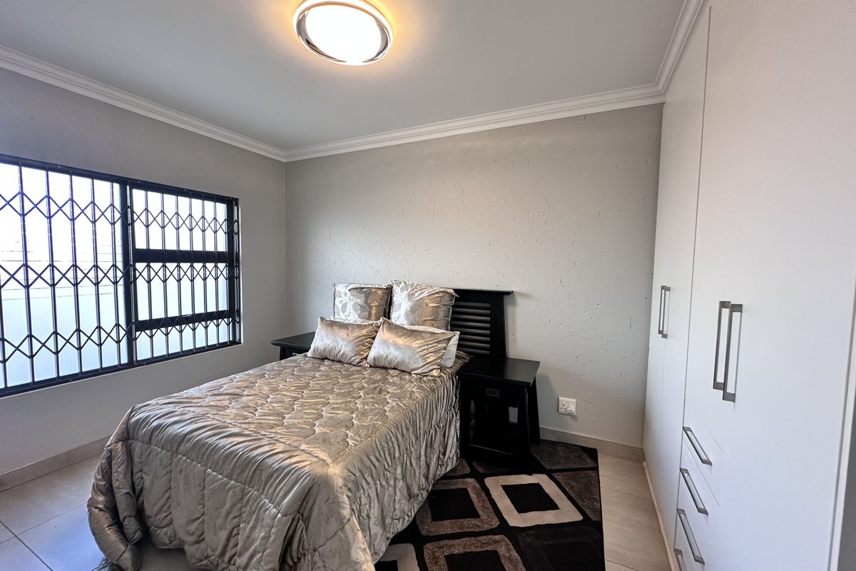 A well-maintained bedroom featuring built-in cupboards, tiled flooring, and a security gate on the window.