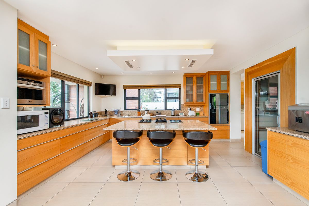 Spacious kitchen featuring light wood cabinetry, granite countertops, a central island with a built-in hob, and integrated appliances including an oven and microwave.