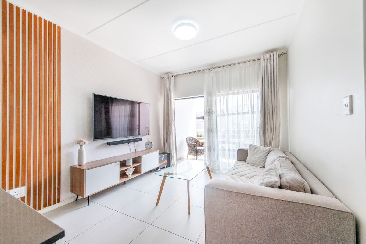 A bright and modern living room featuring tiled flooring, decorative wood slat wall paneling, and sliding glass doors leading to a private balcony.