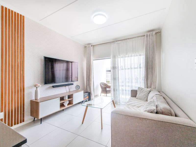 A bright and modern living room featuring tiled flooring, decorative wood slat wall paneling, and sliding glass doors leading to a private balcony.