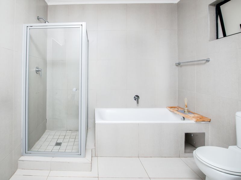 A clean, modern bathroom featuring a separate glass-enclosed shower, a built-in bathtub, and neutral floor-to-ceiling tiling.