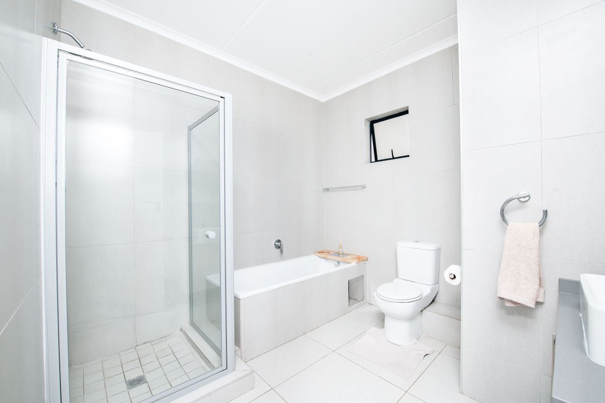 A modern, neutral-toned bathroom featuring a glass-enclosed shower, a built-in bathtub, a toilet, and tiled flooring throughout.