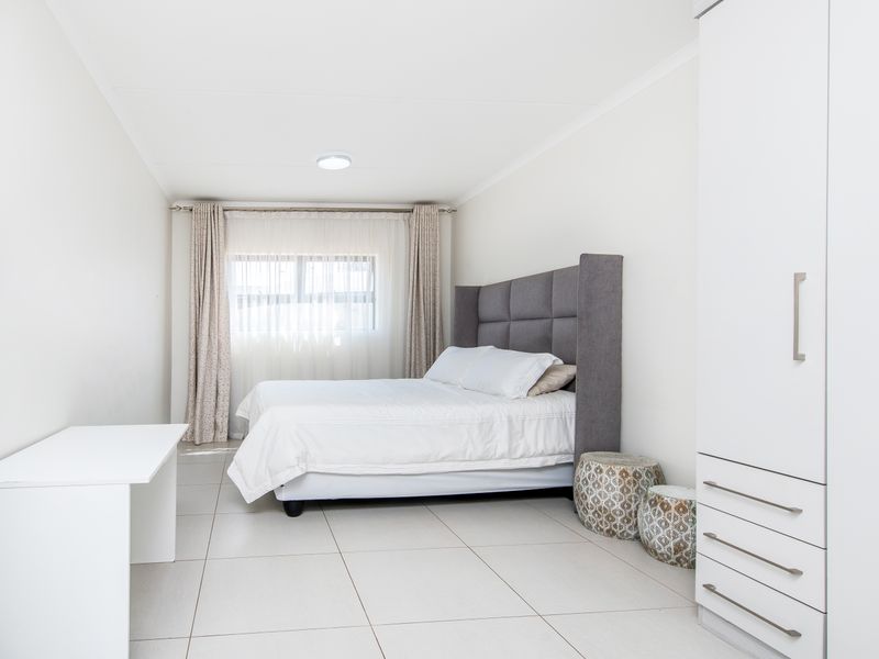 A bright and spacious bedroom featuring neutral tiled flooring, built-in cabinetry, and large windows with curtain tracks.