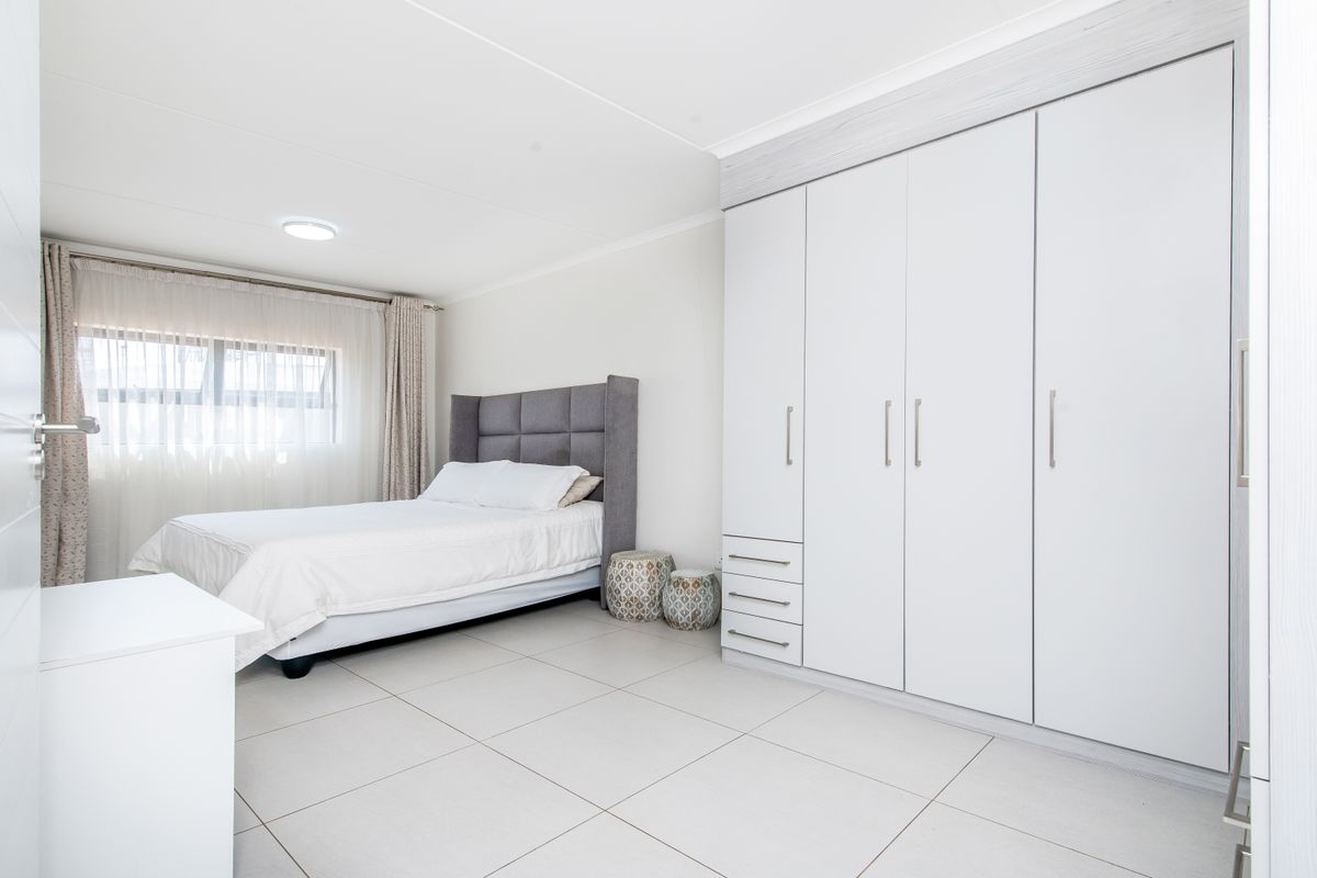 A bright and spacious bedroom featuring large built-in wardrobes with ample storage and neutral tiled flooring.