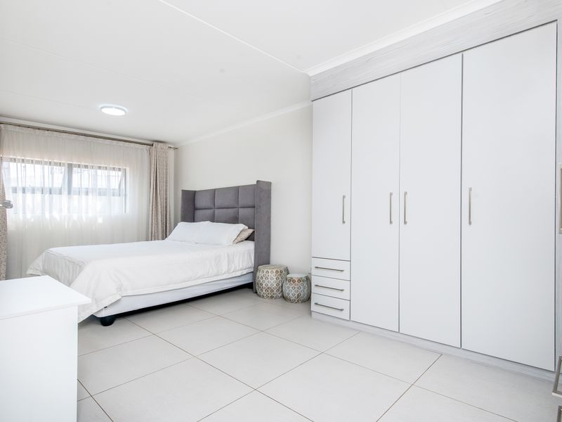 A bright and spacious bedroom featuring large built-in wardrobes with ample storage and neutral tiled flooring.