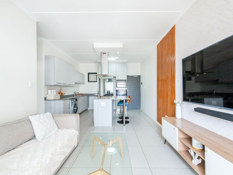 Modern open-plan living area featuring a sleek kitchen with built-in cabinetry, integrated appliances, and a central island, seamlessly flowing into the lounge space.