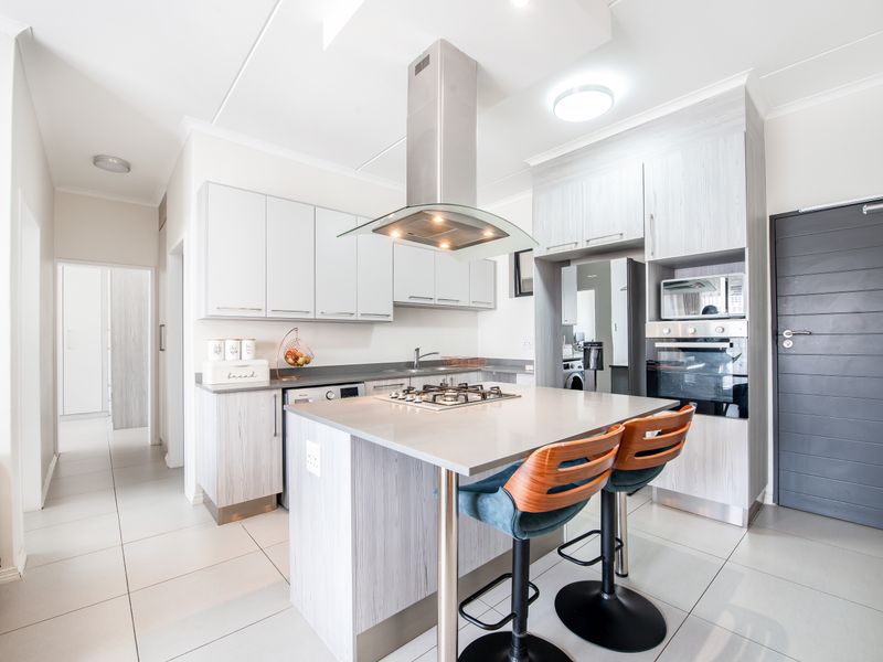 Modern open-plan kitchen featuring light wood-grain cabinetry, a central island with a gas hob, stainless steel extractor fan, and built-in oven.