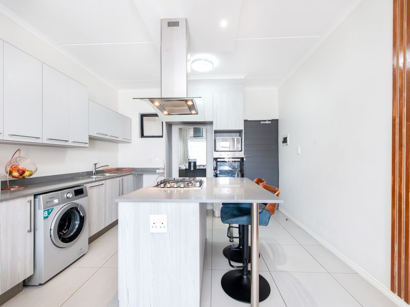 Modern kitchen featuring a central island with a built-in gas hob, stainless steel extractor fan, integrated oven, and sleek cabinetry with tiled flooring.