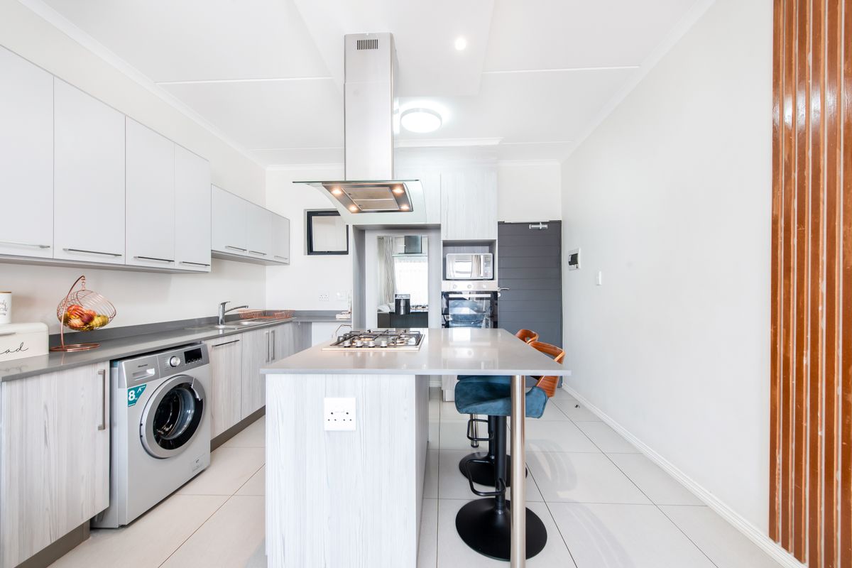 Modern kitchen featuring a central island with a built-in gas hob, stainless steel extractor fan, integrated oven, and sleek cabinetry with tiled flooring.