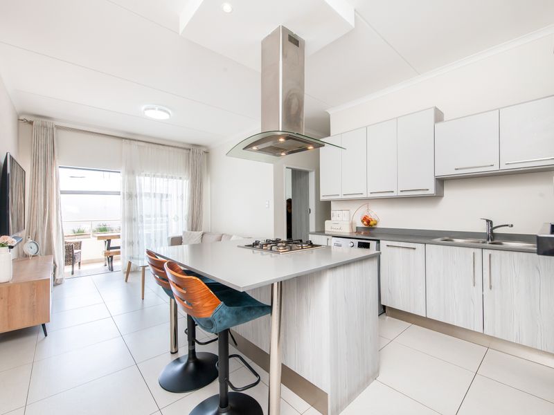 Modern open-plan kitchen and living area featuring a central island with gas hob, stainless steel extractor fan, and light-toned cabinetry.