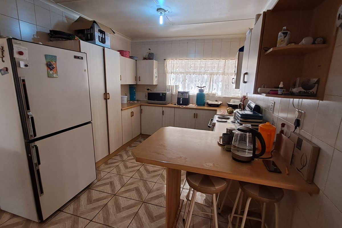 A functional kitchen featuring laminate cabinetry, tiled backsplash, and a built-in breakfast bar, offering a dated aesthetic with potential for modern renovation.