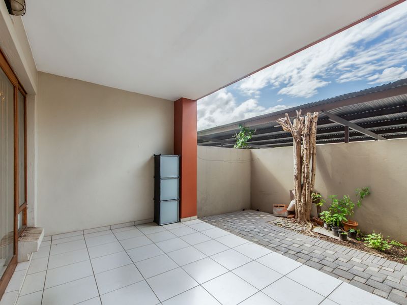 A covered patio area featuring tiled flooring, a paved section, and a sliding door entrance, offering a functional outdoor space.