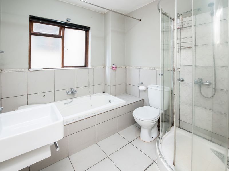 A functional bathroom featuring a built-in bathtub, separate shower enclosure, wall-mounted basin, and toilet with neutral wall and floor tiling.