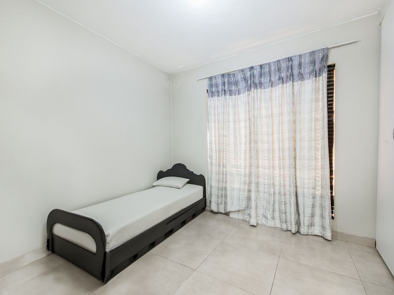 A simple bedroom featuring tiled flooring and a built-in wardrobe, providing a functional and neutral living space.