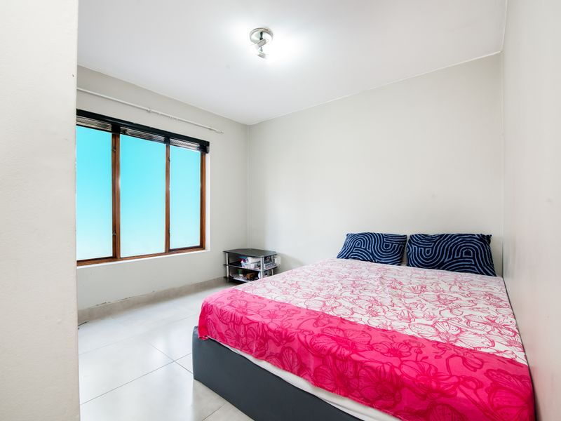 A functional bedroom featuring tiled flooring, neutral walls, and timber-framed windows that provide natural light.