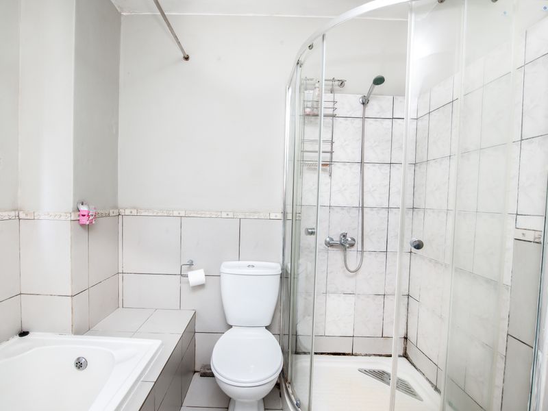 A functional bathroom featuring a built-in bathtub, a separate glass-enclosed shower, and a standard toilet with tiled wall finishes.