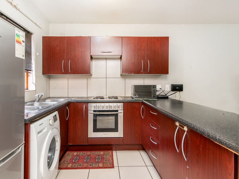 Compact kitchen featuring dark wood-look cabinetry, laminate countertops, tiled backsplash, and integrated oven and hob.