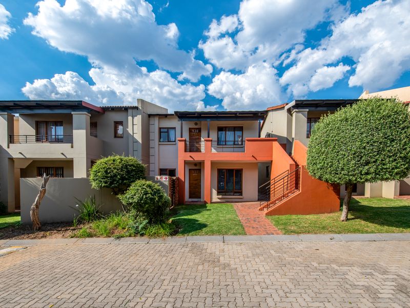 Front elevation of a modern apartment complex featuring brick paving, landscaped gardens, and private balcony and patio access for ground and upper-level units.