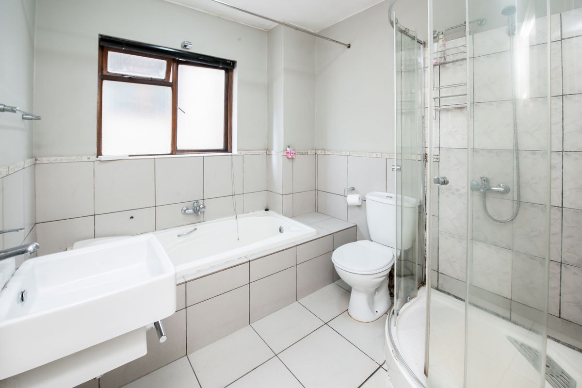 A functional bathroom featuring a built-in bathtub, separate shower enclosure, wall-mounted basin, and toilet with neutral wall and floor tiling.