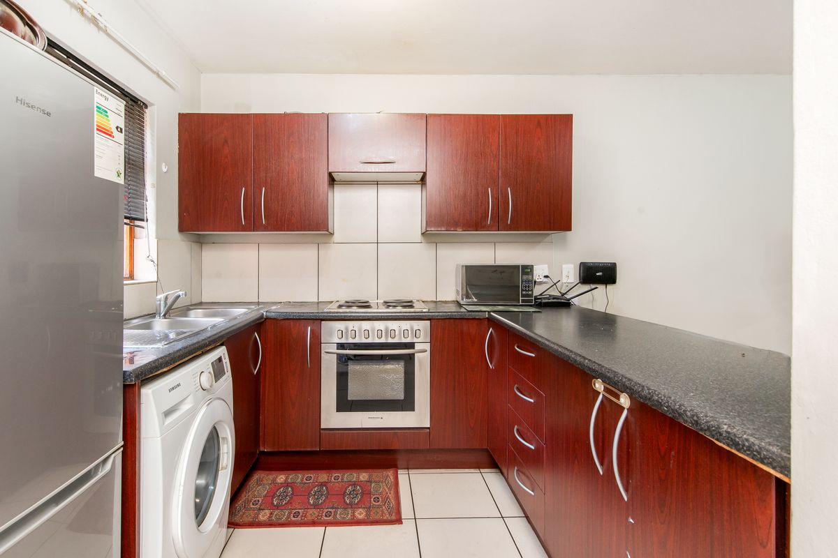 Compact kitchen featuring dark wood-look cabinetry, laminate countertops, tiled backsplash, and integrated oven and hob.