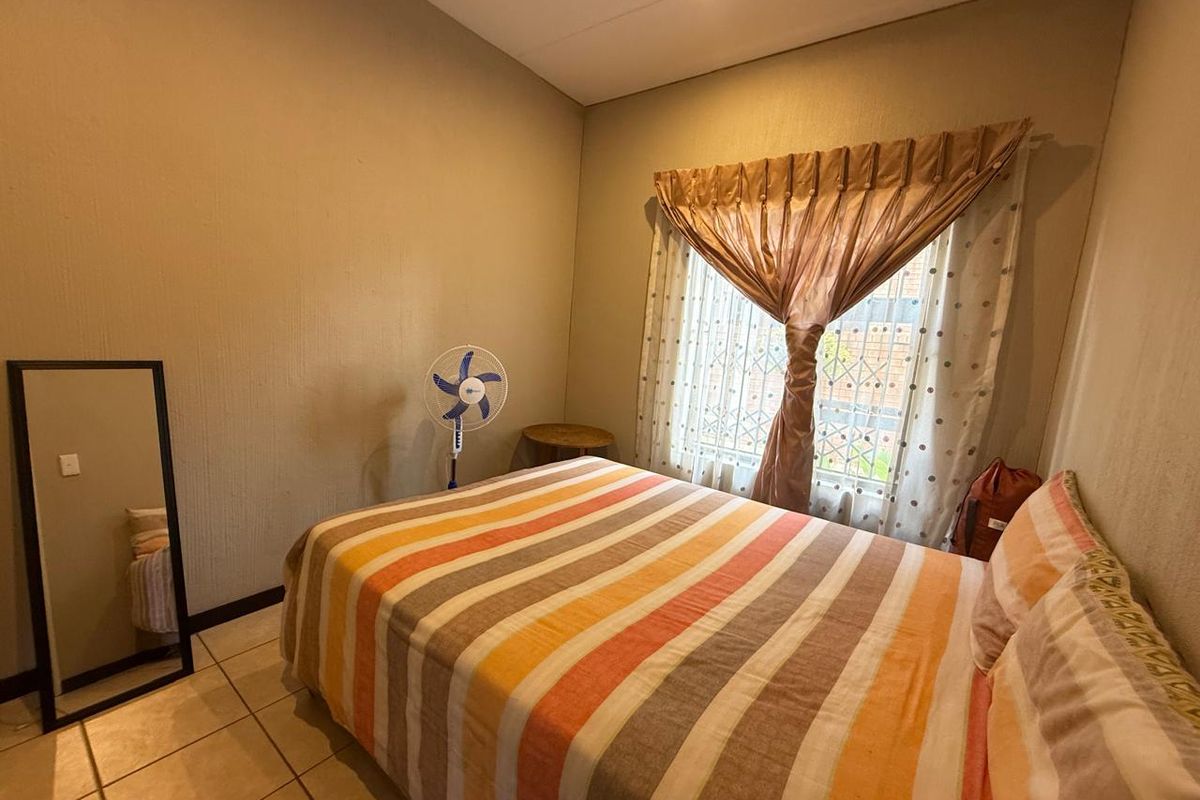 A functional bedroom featuring tiled flooring, recessed lighting, and a window fitted with security bars.