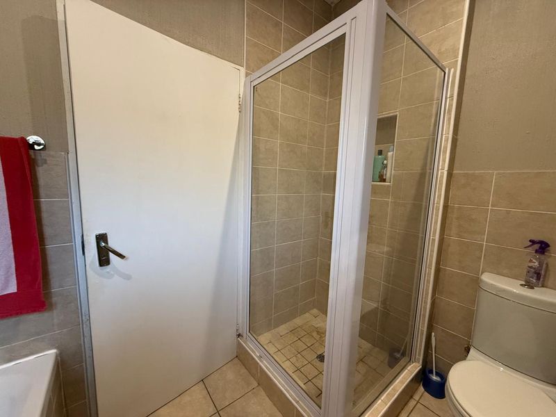 A functional bathroom featuring a glass-enclosed shower with a recessed niche, tiled walls, and standard toilet fixtures.