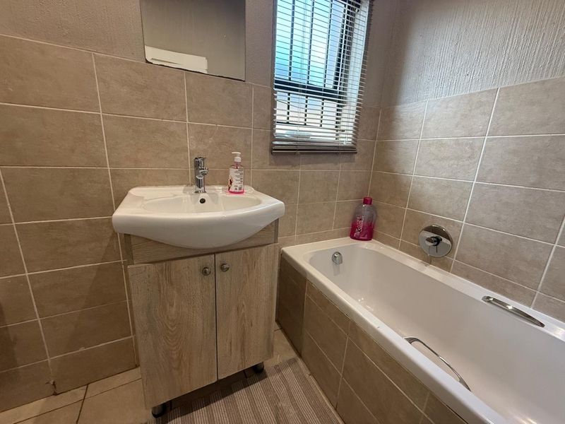 A functional bathroom featuring a built-in bathtub, a vanity cabinet with a basin, and neutral wall tiling.
